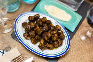 Cooked in shells land snails served on plate with spicy aioli sauce and glass of red wine. Popular dish of Mediterranean cuisine