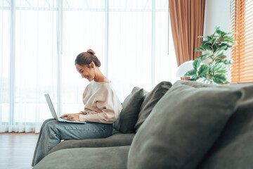 Young Asian beautiful woman relaxing on comfortable couch, using laptop at home, happy girl chatting with friends in social network, spending weekend, watching movie, shopping online