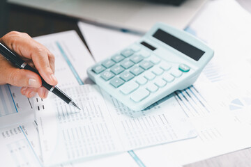 Auditor reviews financial statement and balance sheet on desk using a calculator, representing the...