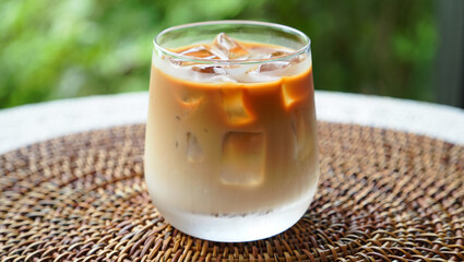 A close-up of an iced coffee latte in a clear glass, filled with ice cubes.