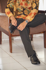 Stylish man adjusting black dress shoes on a chair, wearing patt