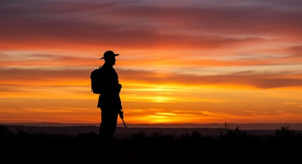Silhouette of a Person with a Backpack Standing in Open Landscape During Vibrant Sunset Sky