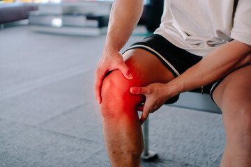A man clutching his knee, seated on a bench. Possible themes: pain, injury, exercise, or sports.