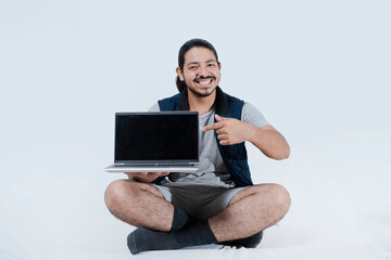 Young man showing computer to camera on white background. Man on the floor showing the computer screen on isolated