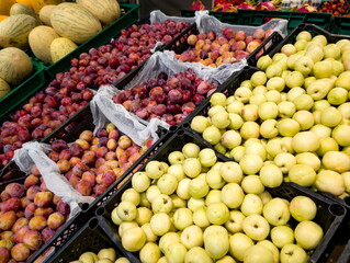 Colorful display of fresh fruits in baskets at an outdoor market during the morning, showcasing multiple varieties of plums and apples