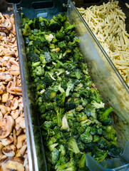 Frozen broccoli with sliced mushrooms and pasta on display in a grocery store produce section during midday hours