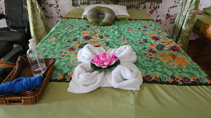 Elegant massage bed setup featuring folded towel art with a pink lotus flower, oils, and fabric on...
