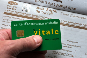 French health insurance card Vitale held above a sick leave certificate form, representing healthcare, insurance, and social security in France.