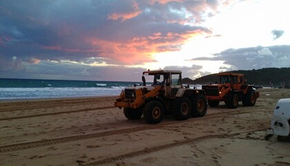 Fototapeta premium A Sunset Beach Scene with Front-End Loaders Industrial Stillness Amid Natural Beauty