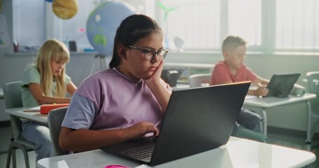 Computer Science Lesson: Primary School Girl Sitting at Desk, Using Laptop in Classroom. Group of Boys and Girls Learning Basic Programming Languages and Internet Safety on Digital Tablets, Laptops. - Powered by Adobe