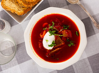 Russian beetroot soup cooked with bone-in beef meat traditionally served with sour cream garnished with greens..