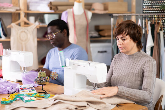 Woman tailor and African male companion sews clothes in sewing machine. Worker uses sewing machine to create clothes for clients.