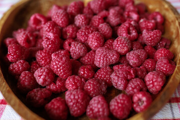 A wooden bowl with ripe raspberries lies on a rustic tablecloth.