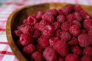 A wooden bowl with ripe raspberries lies on a rustic tablecloth.