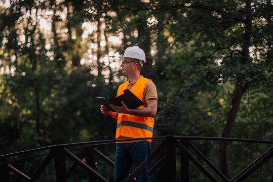 Forest engineer inspecting a wooden bridge in a park, holding a clipboard