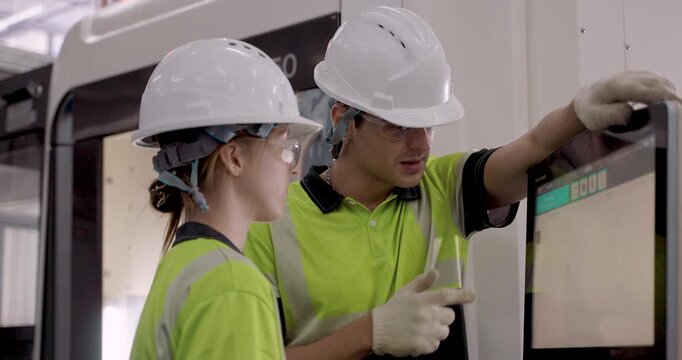 Male instructor pointing to CNC machine interface while explaining function to female trainee during  smart automation training focused on dashboard interaction and industry 4.0  command execution