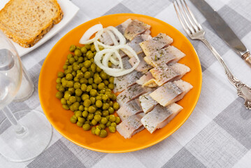 Pieces of herring served with green peas and onions on plate. Appetizer fish on table