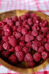 A wooden bowl with ripe raspberries lies on a rustic tablecloth.