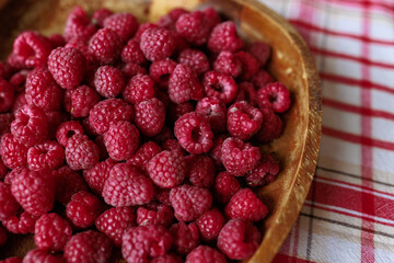 A wooden bowl with ripe raspberries lies on a rustic tablecloth.