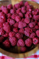 A wooden bowl with ripe raspberries lies on a rustic tablecloth.