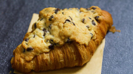 Freshly baked crookie croissant featuring a decadent chocolate chip cookie on top, creating a delightful indulgence, resting on baking paper against a dark table backdrop