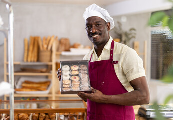 African American man entrepreneur owner of bakery holds out paper bag with pastries in hand, ready...
