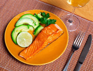 Baked salmon fillet served with fresh avocado and herbs on plate..