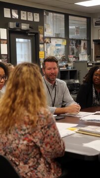 A high school principal welcomes teachers into the administrative office exchanging ideas about new policies and school improvements to enhance student success.