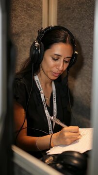 Interpreter adjusting headphones and reading notes while delivering clear live translation in a quiet soundinsulated booth at a multilingual event.