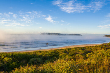 Surfers entering the water at misty Broulee Beach, New South Wales, Australia