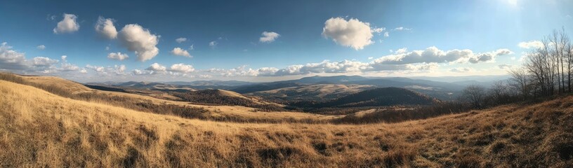 Panoramic view of rolling hills under a partly cloudy sky, golden-brown grasses dominate the foreground, mountains extend to the horizon
