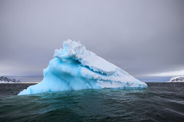 Blue iceberg from a glacier before a storm drifting in the ocean of Svalbard, Norway