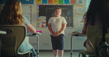 Primary School Boy Showcasing Knowledge of Ecology in Front of Class and Teacher. In Foreground, Two Girls Whispering During Environmental Science Lesson in Classroom. STEM Education. Slow Motion. - Powered by Adobe