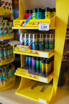 Colorful Clipper lighters displaying multiple designs and colors lined up on vivid yellow shelves inside traditional tabac retail space