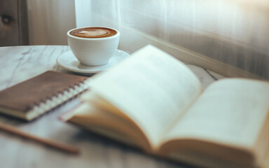 white cup of coffee with latte coffee and leisure reading books, diary, pencil on table by the...