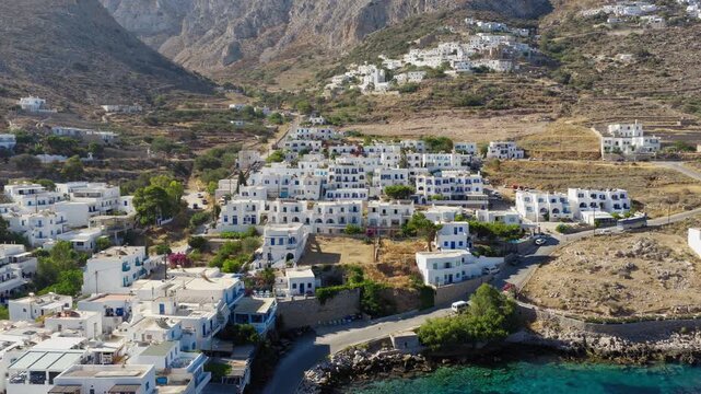 Backwards reveal drone shot uncovering the whitewashed village and port of Aegiali on Amorgos island under bright summer skies