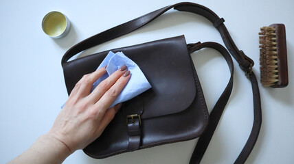 Woman's hand cleaning bag with sponge. Shoulder bag, wallet of crazy horse leather. White...