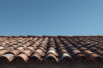 Weathered terracotta roof tiles create a rhythmic pattern against a vast, cloudless blue sky.
