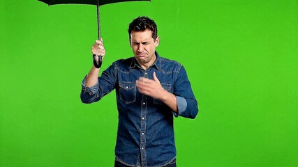 Man in denim shirt looking surprised while holding umbrella handle against a green screen backdrop studio shot