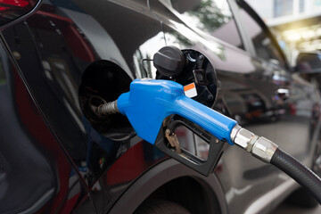Blue gasoline nozzle refueling black car at gas station close up, fuel pump inserted into vehicle...