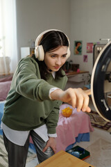 Teenage Caucasian girl wearing headphones adjusting ring light while recording video in bedroom,...