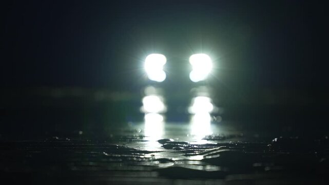 Mysterious car headlights shine through rainy darkness on empty road in cinematic horror atmosphere
