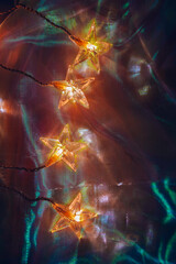 Star-Shaped String Lights on Colorful Background.Christmas garland with glittering iridescent...