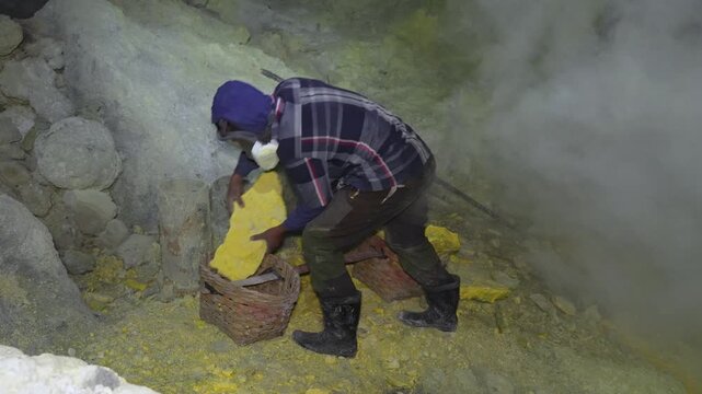 Miner working with sulfur pieces under toxic gas cloud in East Java