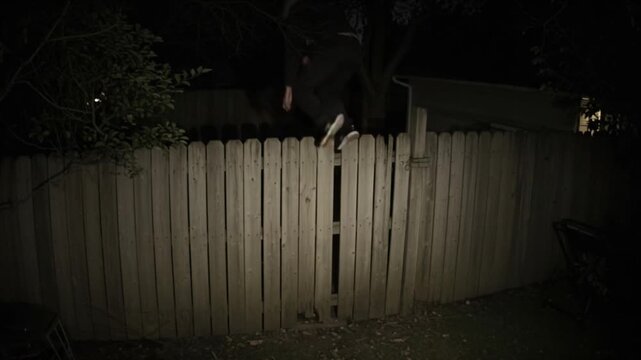CCTV Footage: Suspicious individual scaling wooden fence at night, potentially trespassing in the