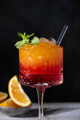 Sunrise cocktail in a tall glass with a straw, pomegranate, orange, crushed ice