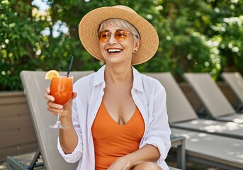Happy senior woman with a cocktail by the pool on a sunny day