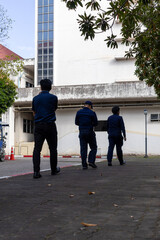 Rear view of three uniformed security guards walking side by side on a city sidewalk during patrol duty. Urban safety teamwork in action.
