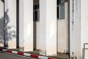 An aged concrete pillar inside an old building illuminated by natural light through a window, casting distinct square-shaped light and shadow patterns.