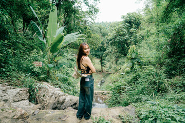 A happy young woman looks back with a charming smile while exploring a lush jungle path. A beautiful and engaging portrait of a traveler enjoying her adventure in a tropical forest.